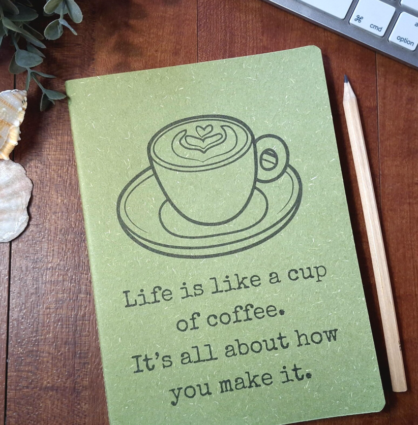 Green notebook with coffee cup illustration and quote on a wooden surface